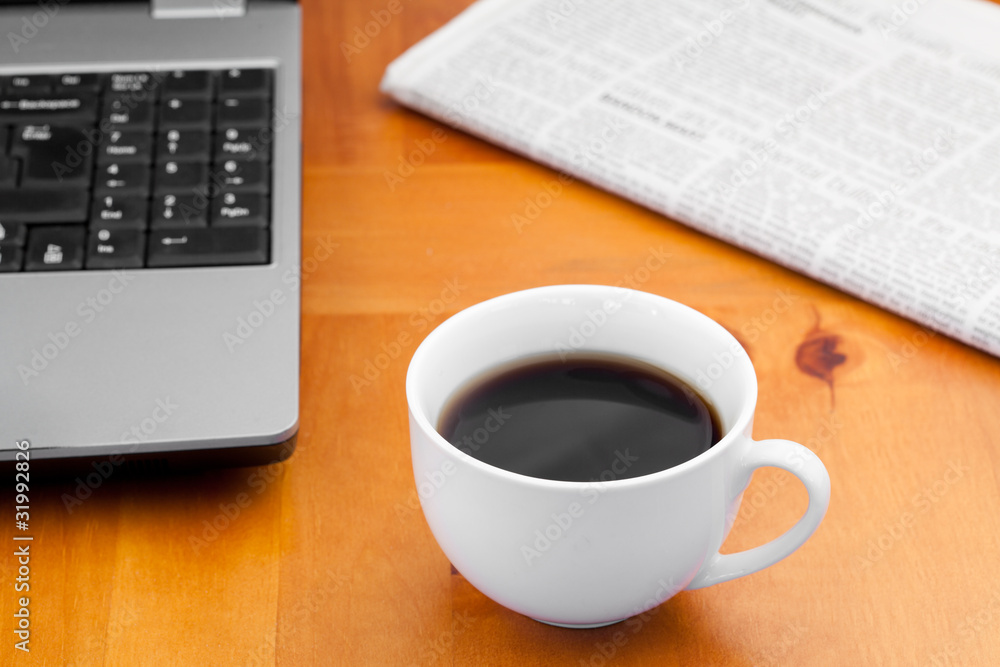 White cup of coffee with laptop and newspaper White cup of coffee with laptop and newspaper