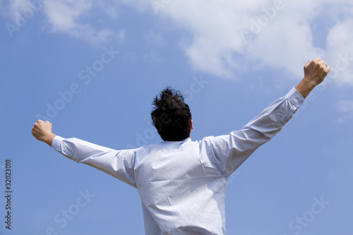 business man with arms outstretched against blue sky