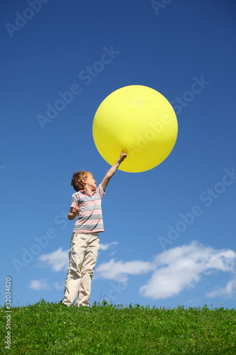 Boy stands in field and lifts yellow balloon and looks at it