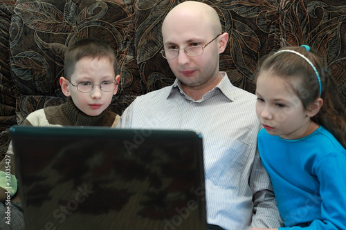 Father, son and daughter sitting on couch and look at laptop photo