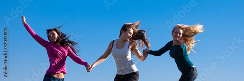 three young beautiful woman jumping into the field against the s