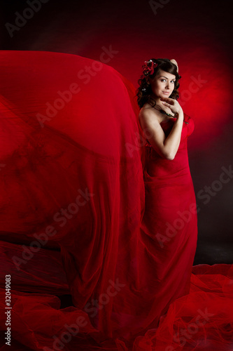 Beautiful woman in red waving flying dress. Looking at camera. © inarik