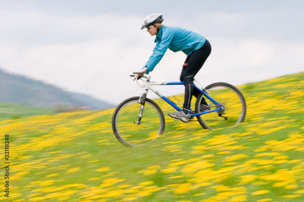 Spring bike riding - woman downhill on bike in dandelion Spring bike riding - woman downhill on bike in dandelion