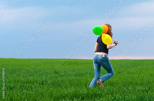 Woman running away with yellow baloons on the green field