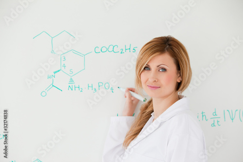 Female scientist looking at the camera while writing a formula o