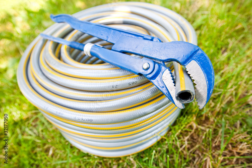 Blue metall spanner and plastic hose on green grass photo