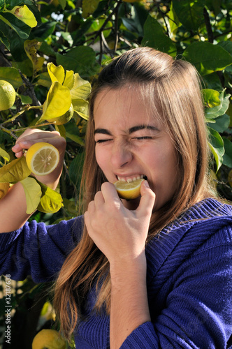 Girl eating a lemon from the tree.