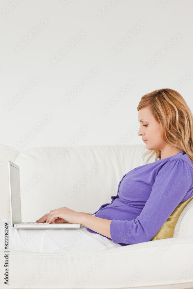 Good loooking red-haired woman using a laptop while lying on a s Good loooking red-haired woman using a laptop while lying on a s