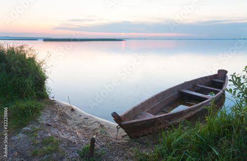 Sunset with old flooding boat on summer lake shore