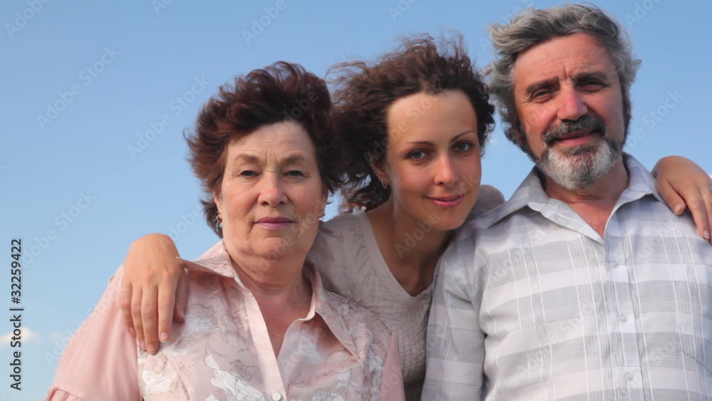 couple stands embracing with adult daughter against sky couple stands embracing with adult daughter against sky