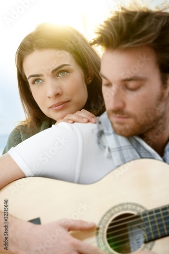 Romantic couple sitting playing guitar outdoor ó