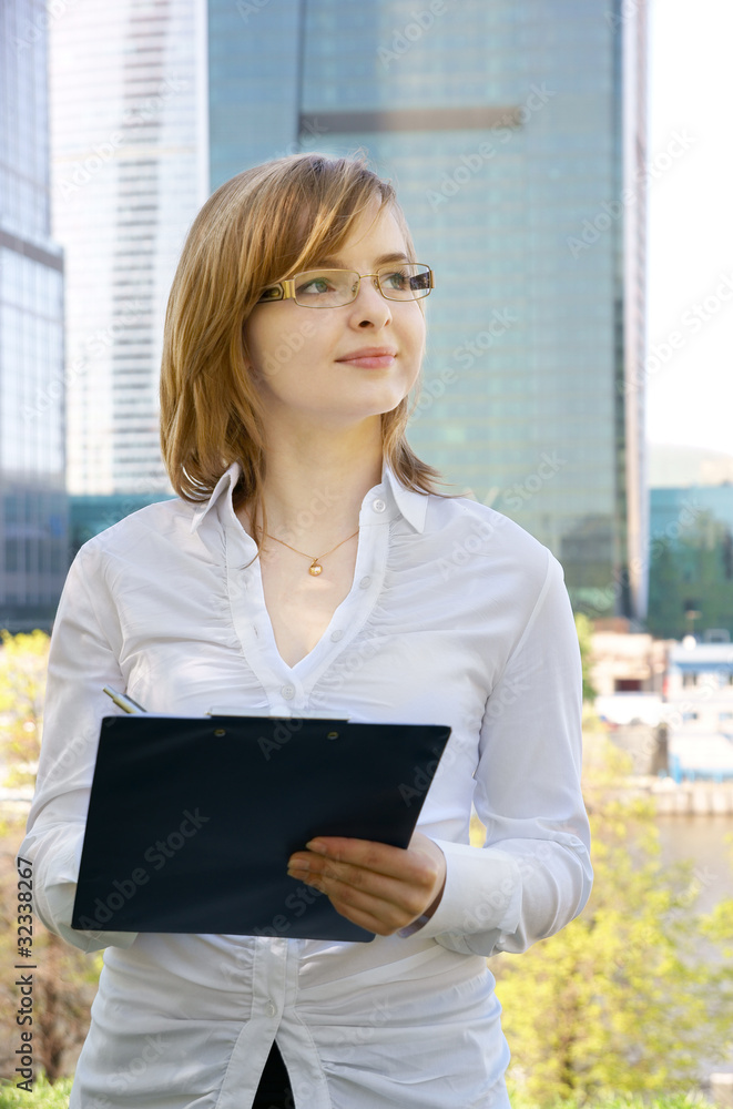 Fototapeta premium Young business woman with clipboard on building background