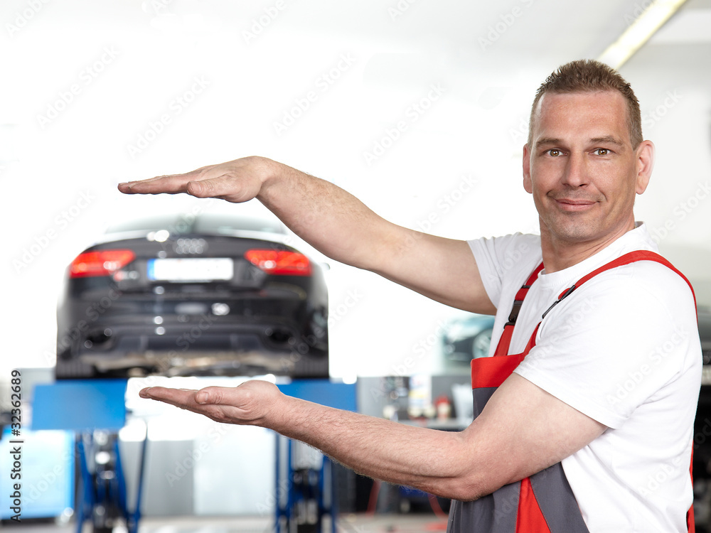 Car mechanic in a garage holding his hands over and among a car Car mechanic in a garage holding his hands over and among a car