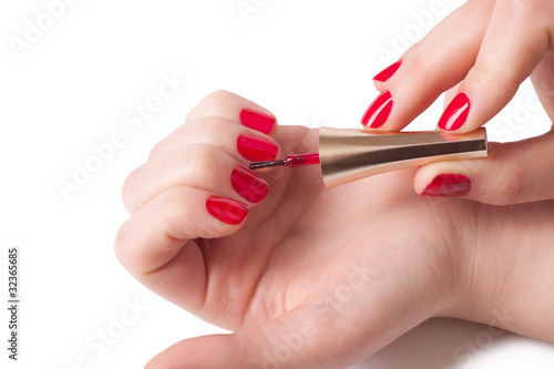 Manicurist applying red nail polish on female fingers