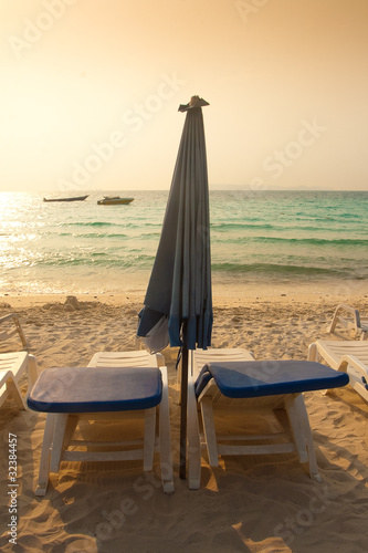 Two sun beds for sunbathing with a blue umbrella on the beach