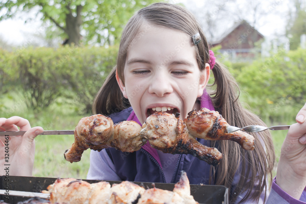 Teen girl bites grilled meat outdoors