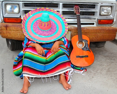 Man wearing sombrero and poncho resting in front of a truck