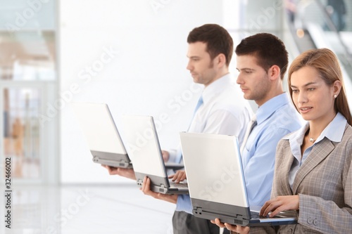 Young professionals using laptop in office lobby