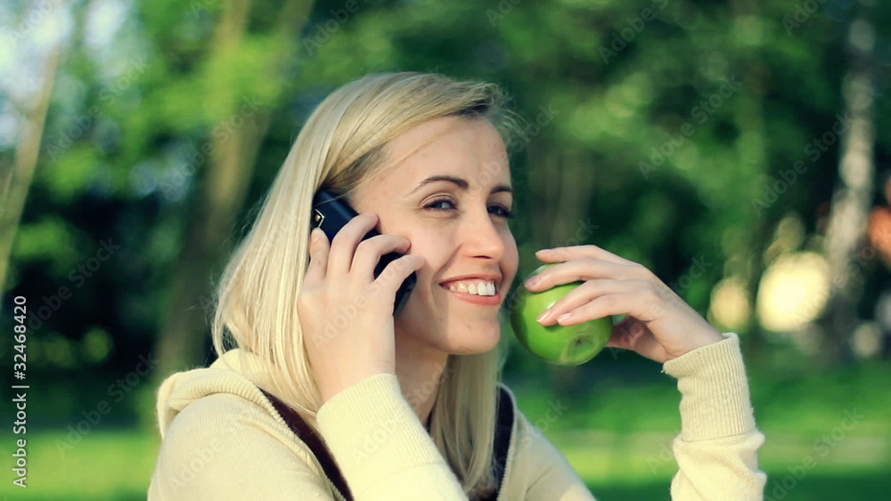 Happy woman holding apple and talking on mobile phone, outdoors Happy woman holding apple and talking on mobile phone, outdoors