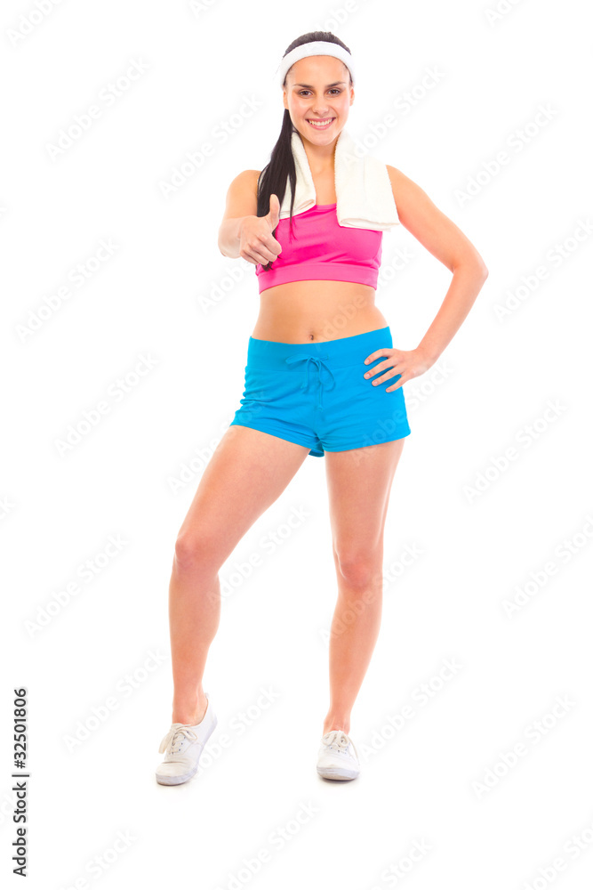 Smiling fitness girl with towel around neck showing thumbs up Smiling fitness girl with towel around neck showing thumbs up