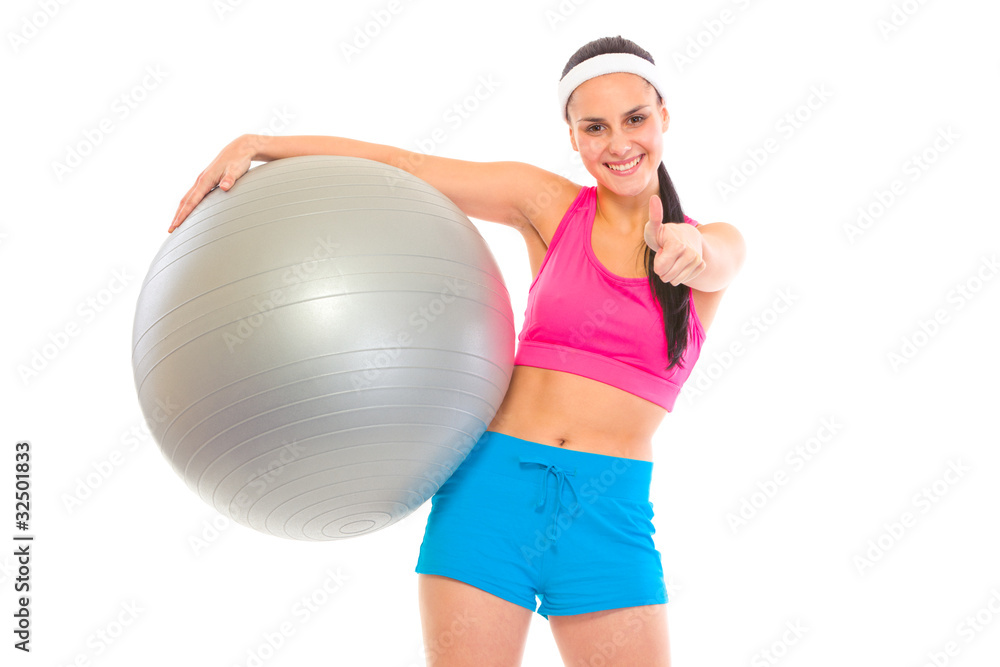 Smiling fit young girl with fitness ball showing thumbs up Smiling fit young girl with fitness ball showing thumbs up