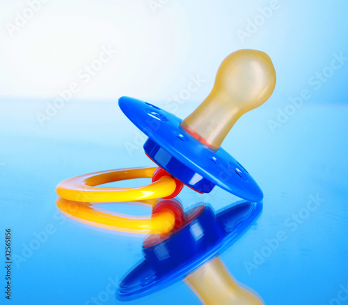 Baby silicone pacifier in blue, red and yellow  colors  on blue