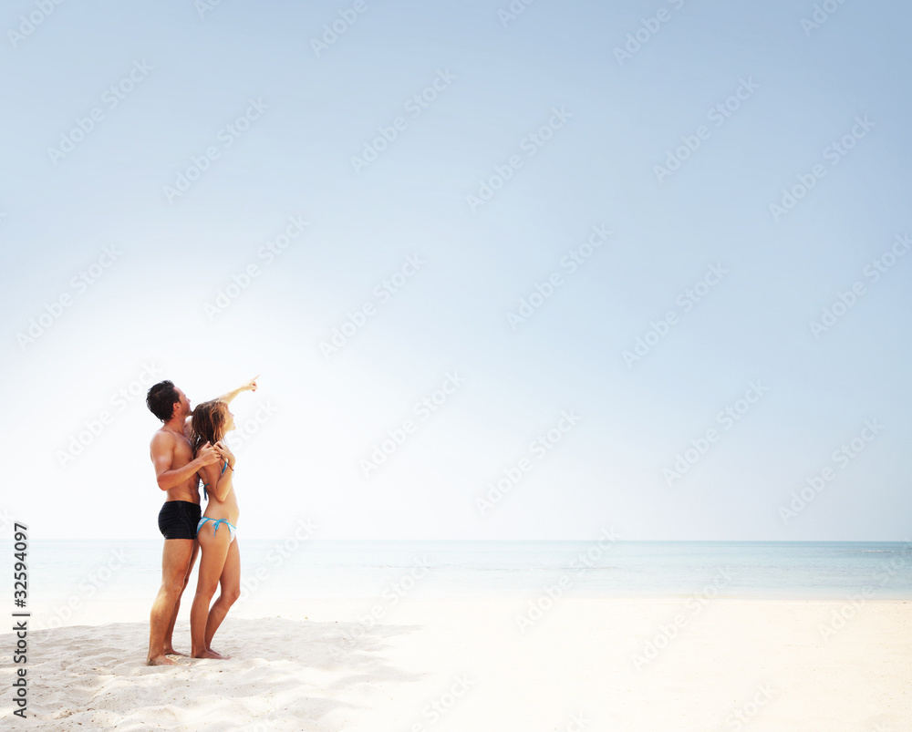 Young couple standing together on the white sand and looking to a blue clear sky