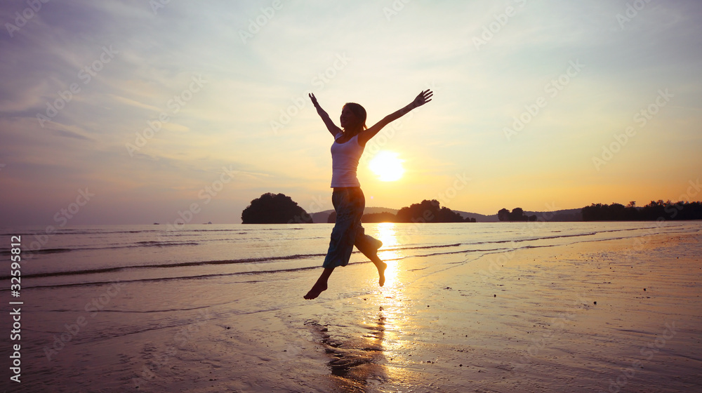 Young woman with raised hands running on wet sand