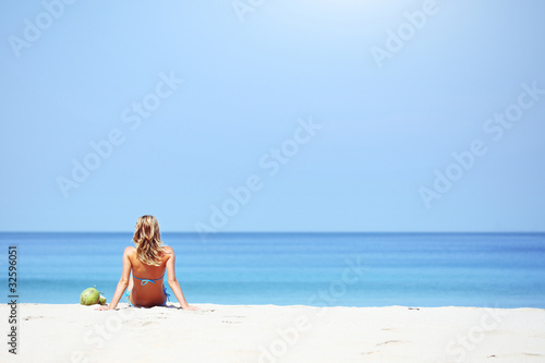Young woman sitting on sand and looking to a sea