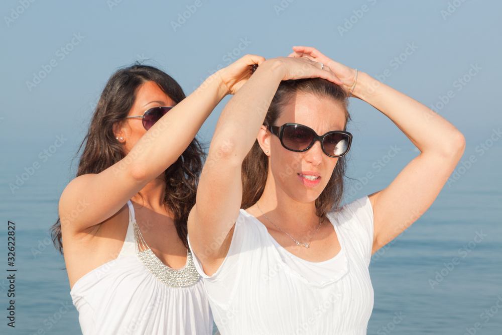 Young Woman Dress Her Friend's Hairs at Seaside Young Woman Dress Her Friend's Hairs at Seaside