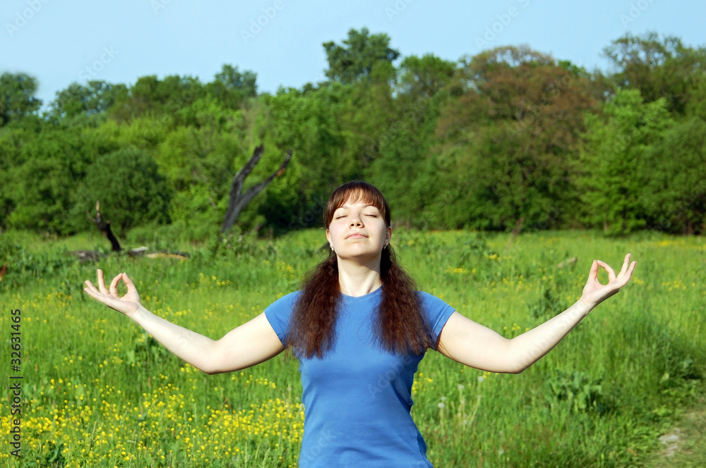 Young happy woman training yoga on green meadow