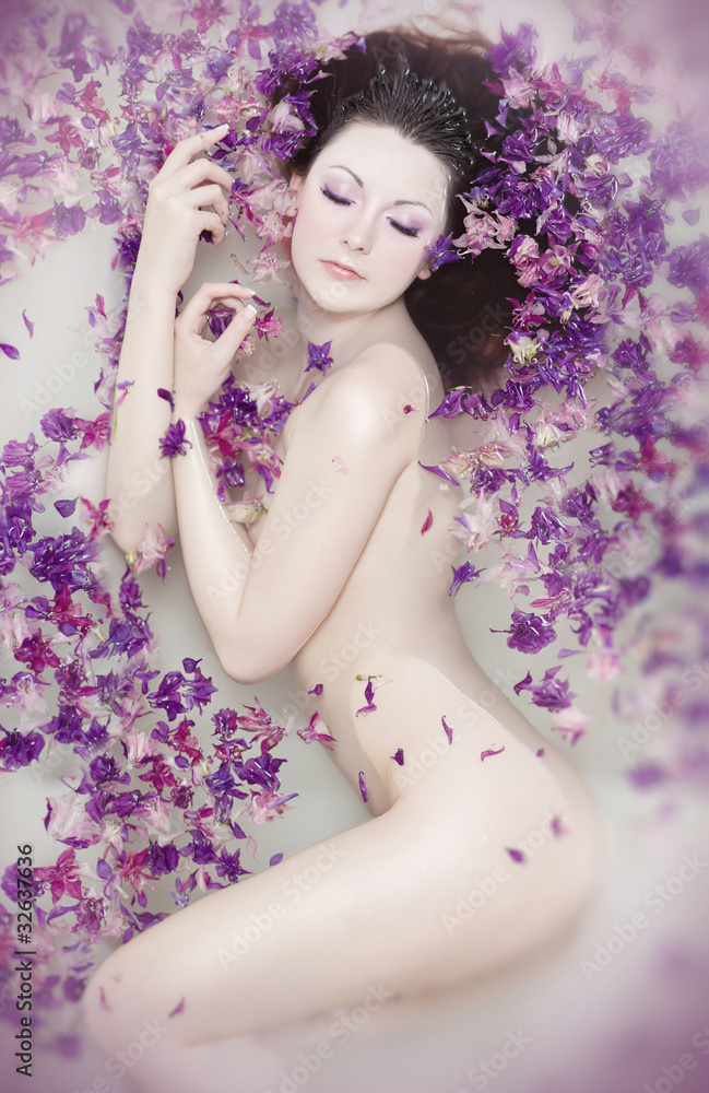 Attractive naked girl enjoys a bath with milk and rose petals.