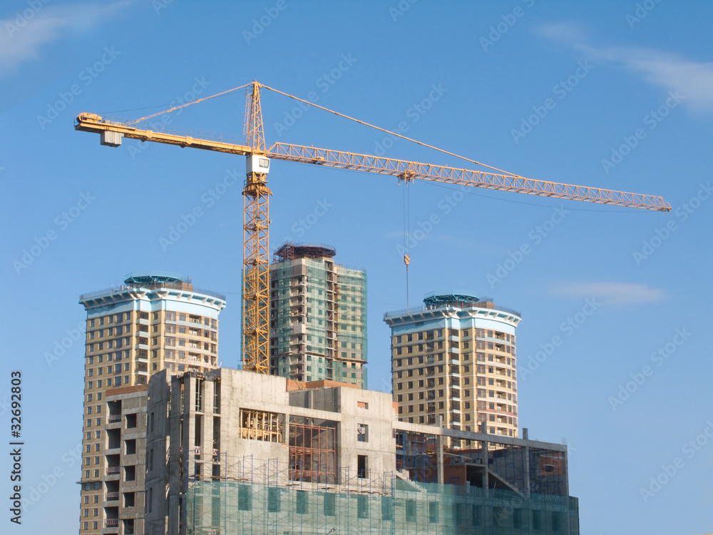 Yellow hoisting crane and some constructing buildings