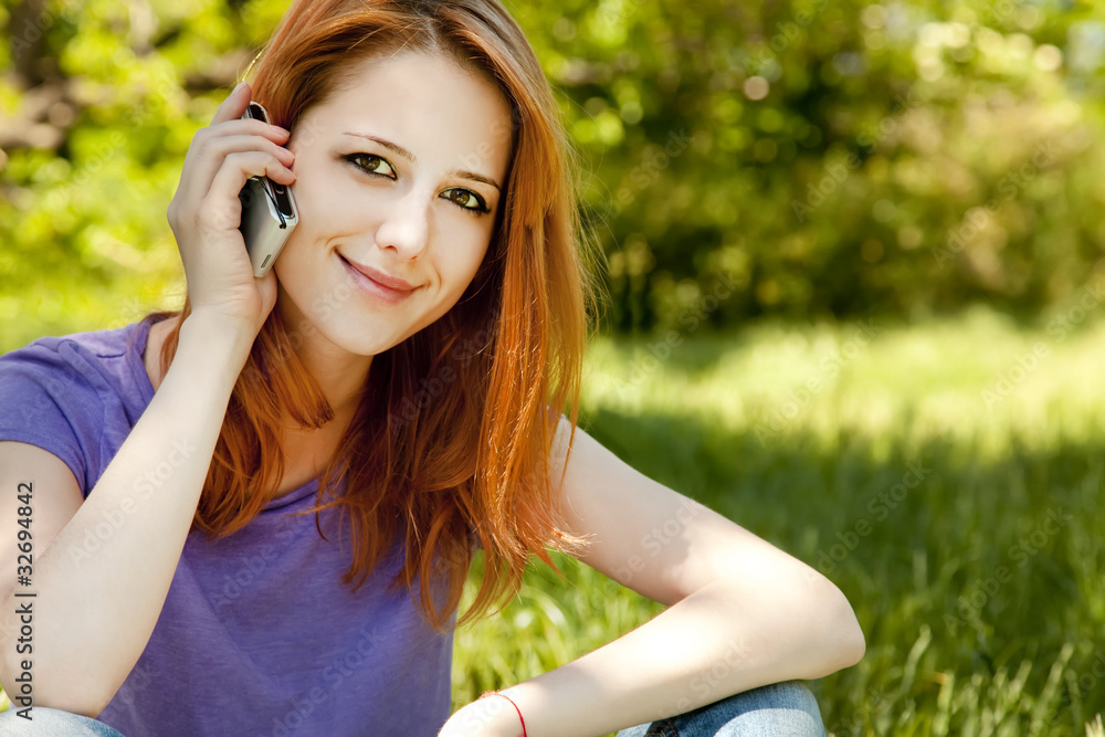 Beautiful redhead girl with mobile phone at the park in summer t