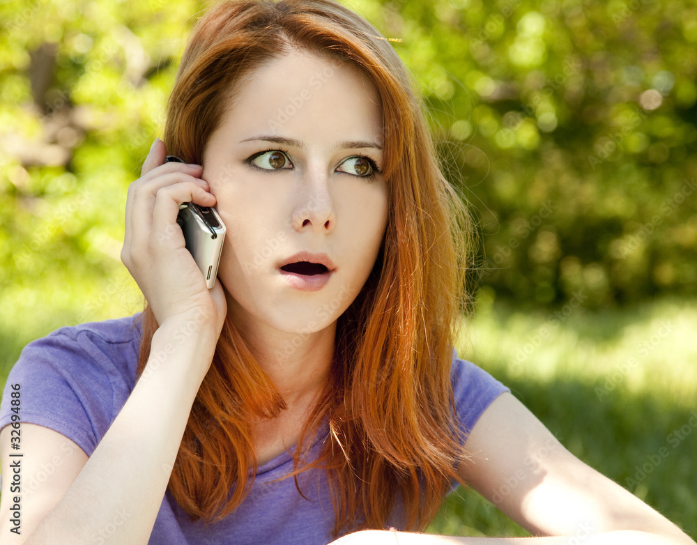 Surprised redhead girl with mobile phone at the park in summer t Surprised redhead girl with mobile phone at the park in summer t