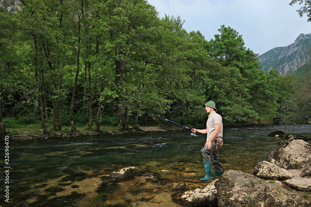 Young fisherman fishing on a river with trees in the background