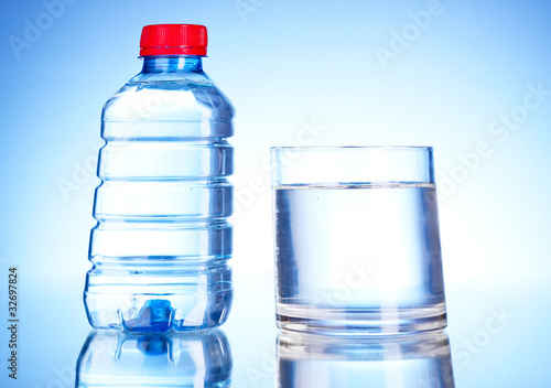 Bottle of water and glass on blue background