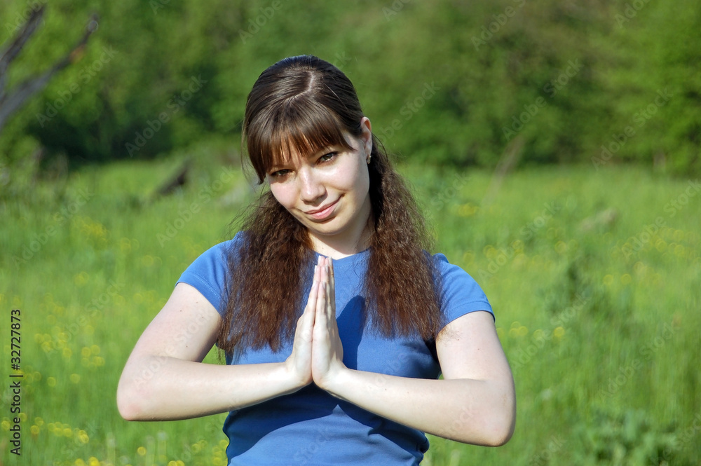 Young happy woman training yoga on green meadow