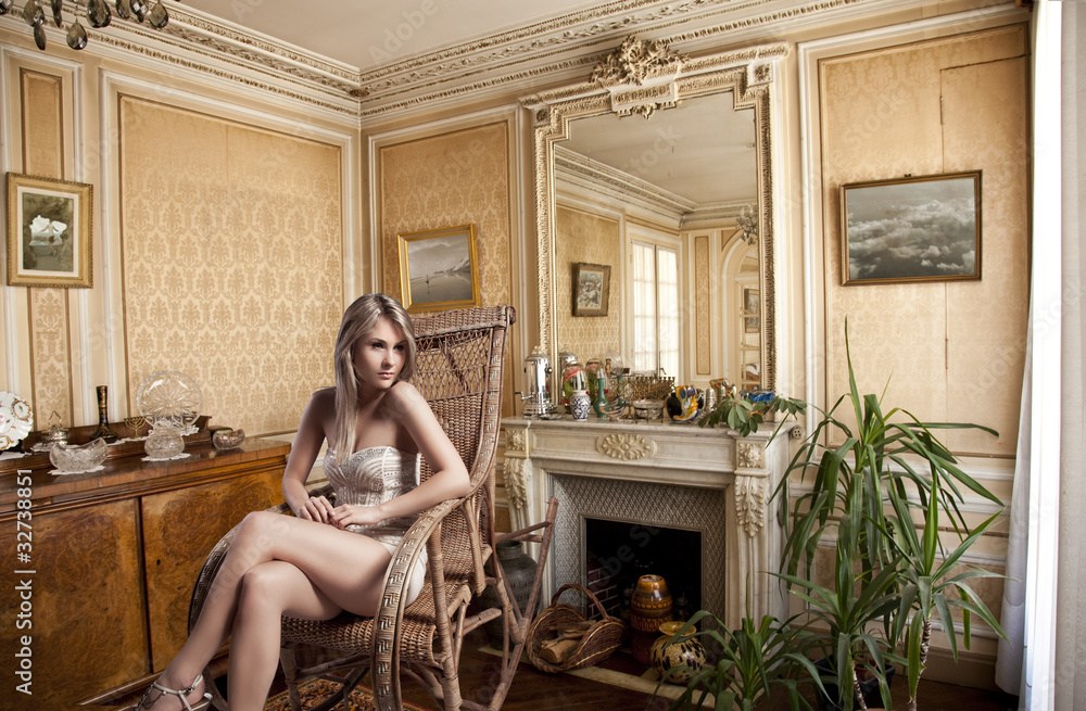 blond girl sitting in a rocking chair near the fireplace - obrazy, fototapety, plakaty 