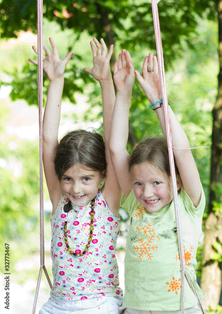 Two happy girls together on the swing - playing outdoor Two happy girls together on the swing - playing outdoor