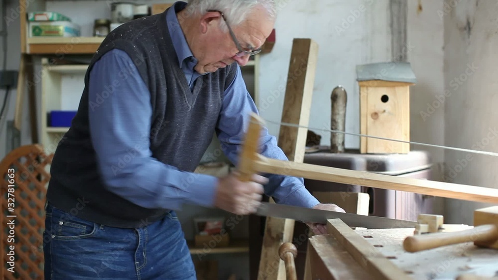 älterer mann sägt holzbalken in der werkstatt älterer mann sägt holzbalken in der werkstatt