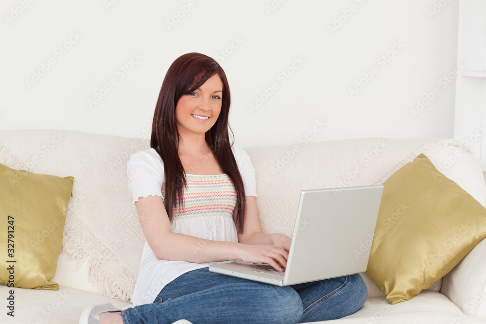 Attractive red-haired woman relaxing with her laptop while sitti Attractive red-haired woman relaxing with her laptop while sitti