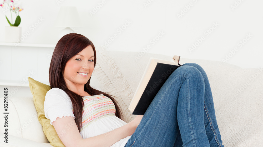 Beautiful red-haired woman reading a book while lying on a sofa Beautiful red-haired woman reading a book while lying on a sofa