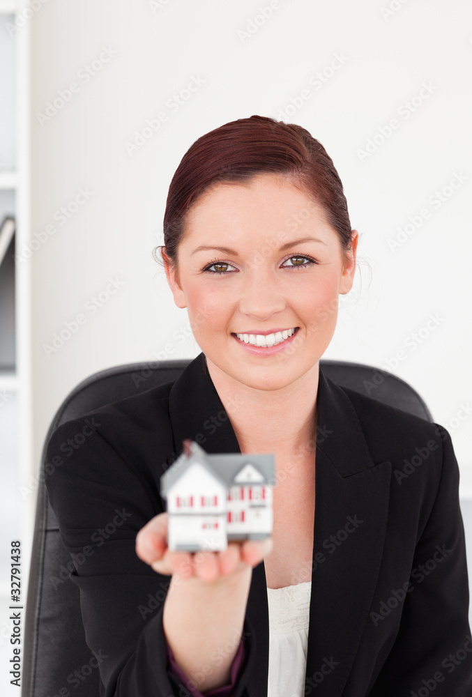Attractive red-haired woman in suit holding a miniature house Attractive red-haired woman in suit holding a miniature house