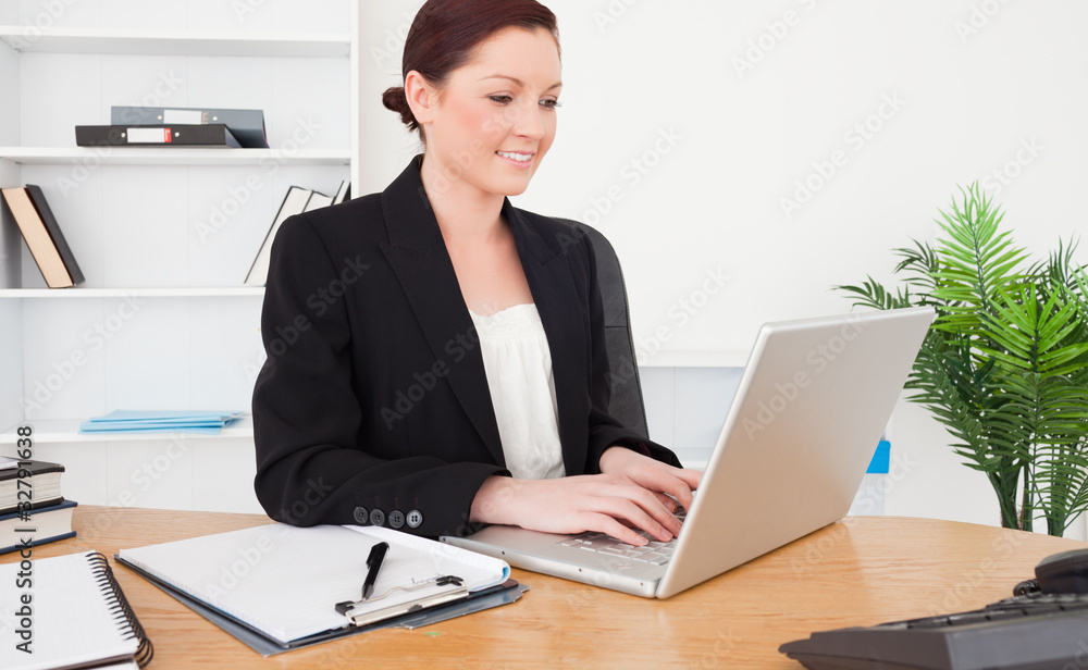 Young attractive red-haired female in suit typing on her laptop Young attractive red-haired female in suit typing on her laptop