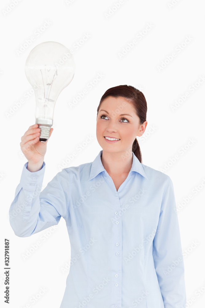 Attractive red-haired female holding a light bulb while standing Attractive red-haired female holding a light bulb while standing