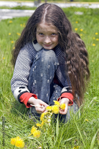 girl sits on a lawn with yellow dandelions photo