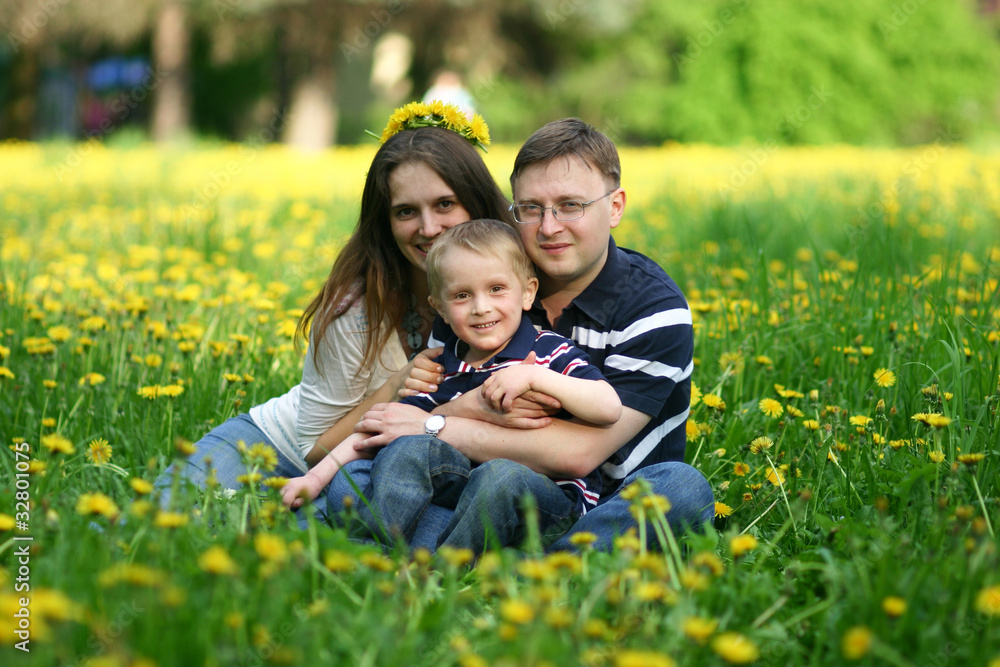 Fototapeta premium Happy young family of three on field of dandelions