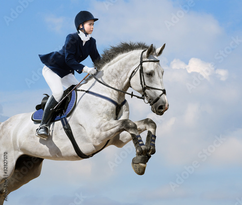 Obraz na plátne Equestrian jumper - young girl jumping with dapple-grey horse