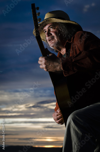Guitar player with straw hat in dramatic lighting